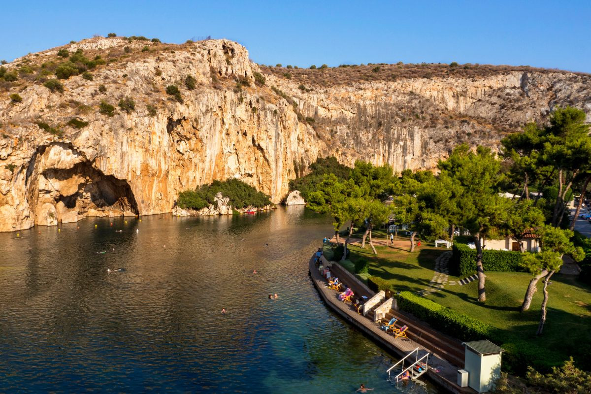 The serene Lake Vouliagmeni surrounded by rocky cliffs and lush greenery with people relaxing and swimming.